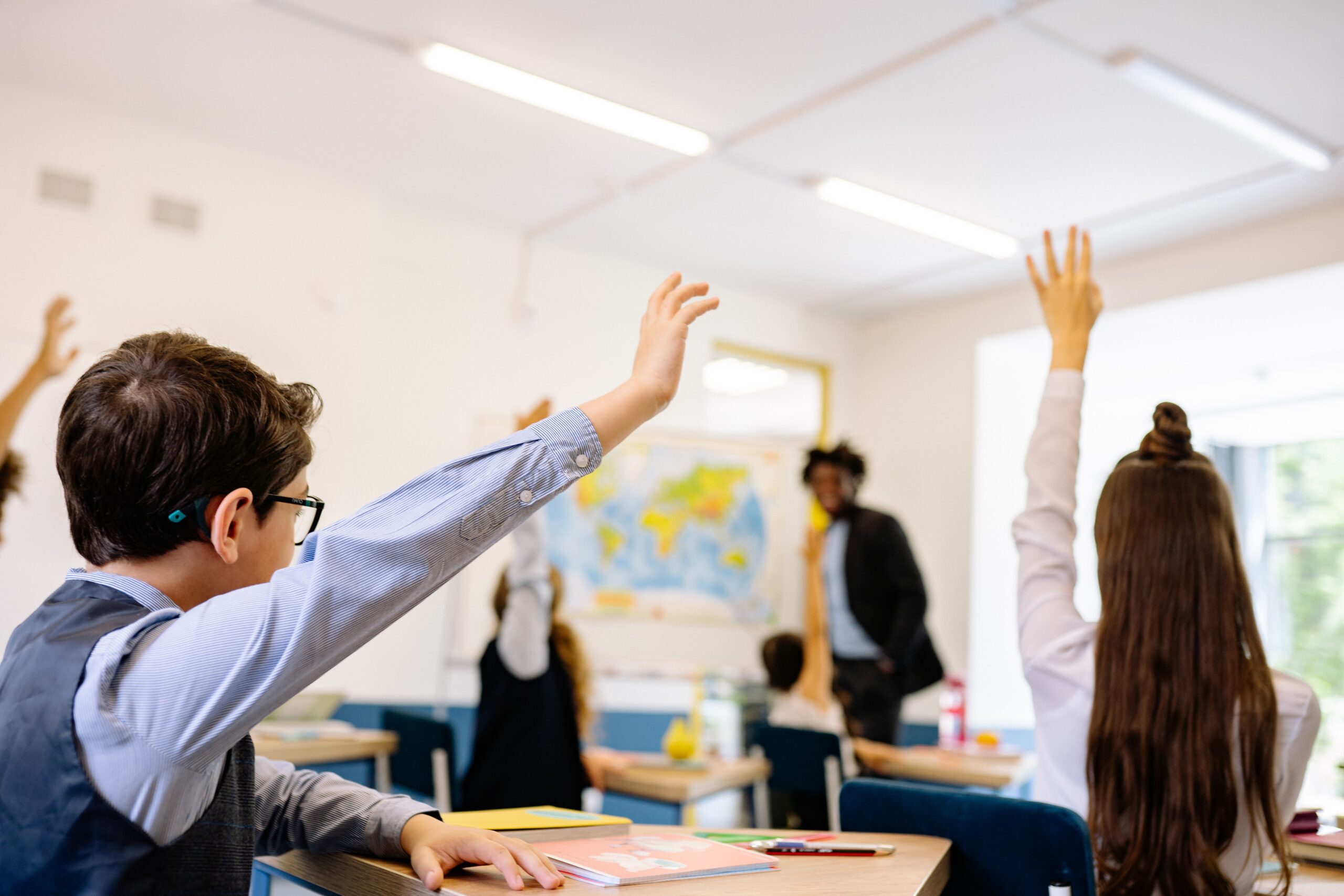 a teacher in the classroom with children raising their hands